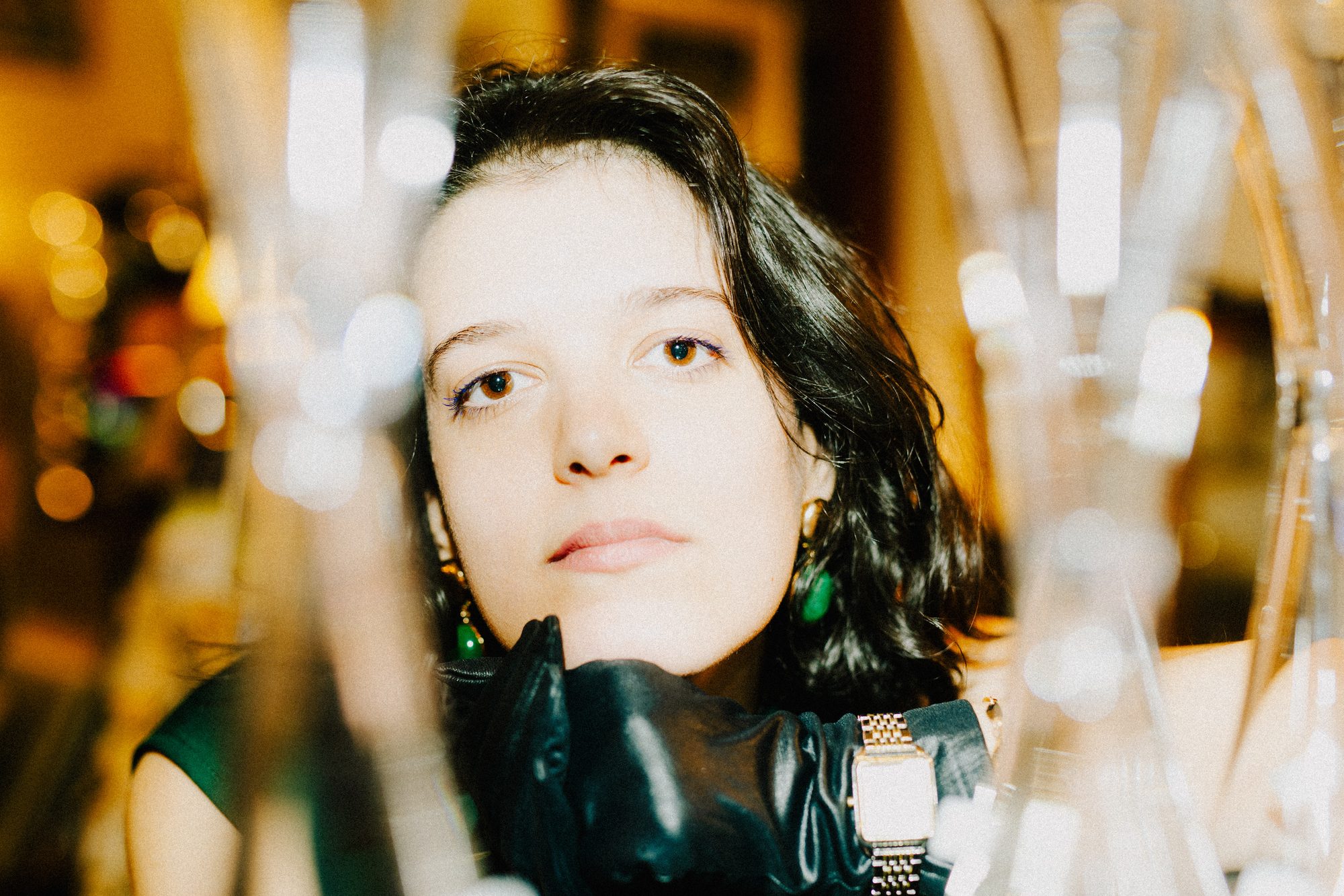 Patrícia Pinheiro photographed behind hanging glassware, looking up past the camera